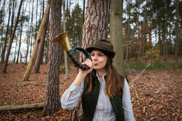 Brauchtum bei der Jagd, junge Jägerin mit einem Jagdhorn im Jagdrevier - jagdliches Symbolfoto.