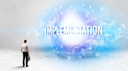 Rear view of a businessman standing in front of IMPLEMENTATION inscription, modern technology concept