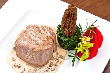 Beef steak with morel sauce, decorated with rose petals and parsley on a plate on wooden background