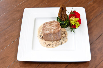 Beef steak with morel sauce, decorated with rose petals and parsley on a plate on wooden background