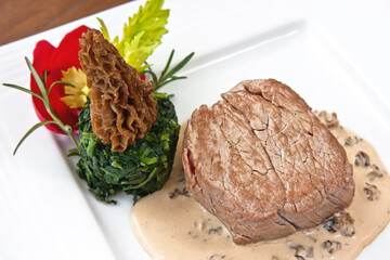 Beef steak with morel sauce, decorated with rose petals and parsley on a plate on wooden background
