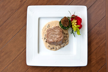 Beef steak with morel sauce, decorated with rose petals and parsley on a plate on wooden background