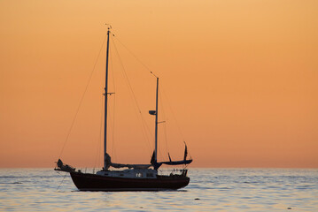 Silhouette of a sailboat at sunset against an orange sky in corona del mar beach in orange county California