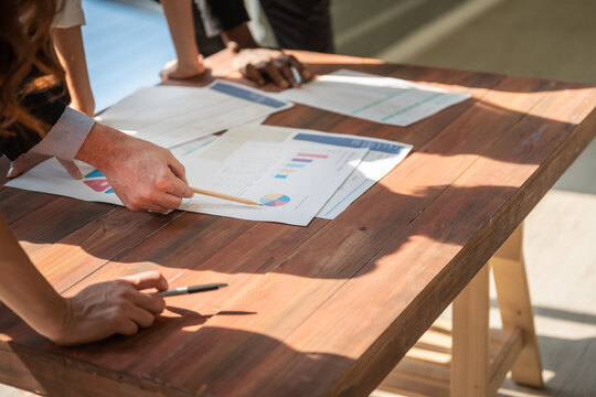 Business Meeting And Communication Concept. Closeup Of Businessman Hand Holding Pencil And Pointing To Pie Chart Report Paper On Wooden Table.