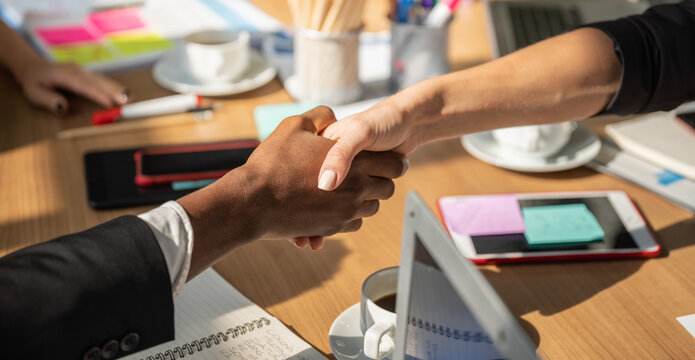 Business Meeting and Communication Concept. Closeup of businessman and businesswoman make a hand shaking in woking office desk with laptop computer, tablet, smartphone and notebook.