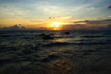beautiful golden sunset over wavy dark sea with clouds on the blue sky