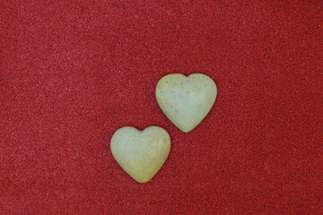 Obraz premium Two polished light stones, carved in the shape of a heart, lie on a beautiful red fabric with sequins. Valentine's Day and love symbol. Flat lay. Copy space, holiday card