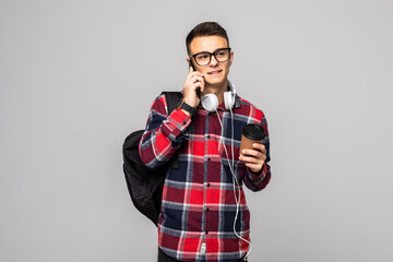 Smiling student with bag holding books and talking on a phone isolated on gray background