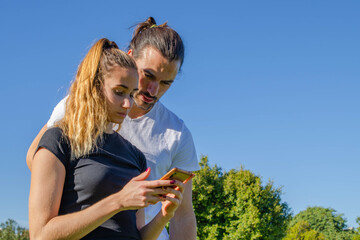 Young Attractive Couple in Sportswear Tracksuit Looking Serious at her Mobile Phone at the Park...