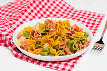 Ready-made Italian pasta with hearts in a white plate on a checkered white-red tablecloth and sprinkled with grated cheese. Valentine's day dinner.