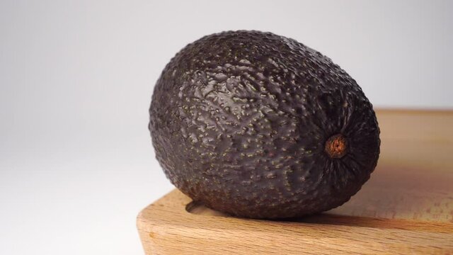 One avocado with pimpled skin on a wooden board on a white background. Diet ripe whole unpeeled vegetable close up