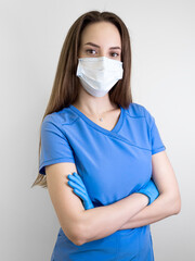 portrait of a young woman nurse in a blue medical uniform, protective mask and gloves on a gray background