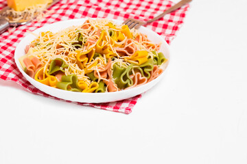 Ready-made Italian pasta with hearts in a white plate on a checkered white-red tablecloth and sprinkled with grated cheese. Valentine's day dinner.