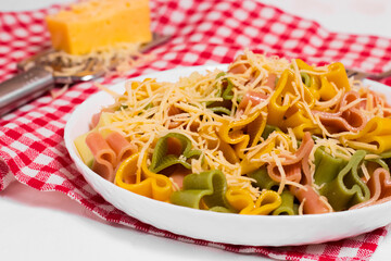 Ready-made Italian pasta with hearts in a white plate on a checkered white-red tablecloth and sprinkled with grated cheese. Valentine's day dinner.