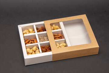 The box on a dark background for nuts is divided into cashews, almonds, raisins and sunflower seeds, selective focus.