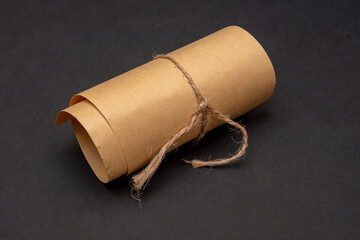 A twisted roll of yellow paper with smooth edges, tied with a rough rope on a dark background, a selective focus.