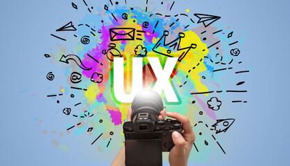 Close-up of a hand holding digital camera with abstract drawing and UX inscription