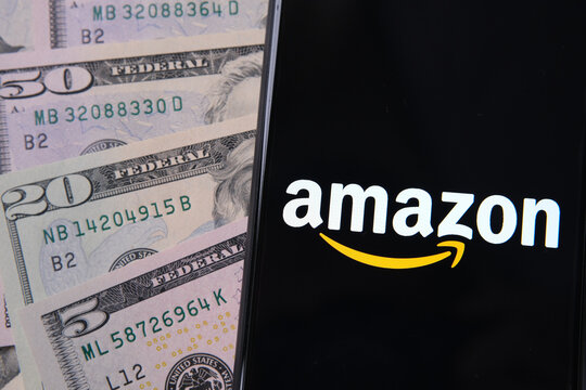 Amazon logo on smartphone placed next to dollar banknotes.