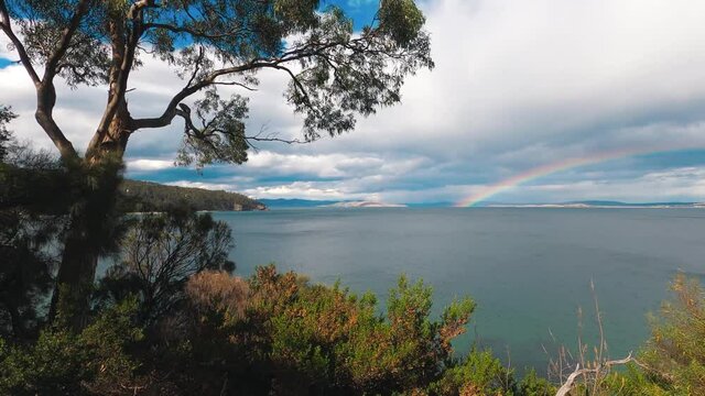 rainbow and stormy skies surroundd by a pristine wild landscape at Boronia Beach Track in Tasmania, Australia with lush vegetation