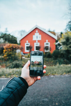 A vertical closeup shot of a person taking a photo of a traditional red house
