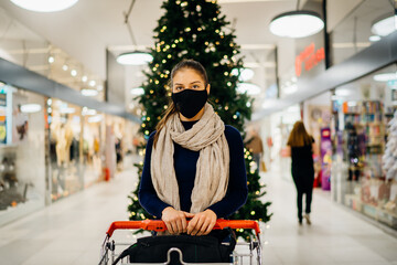 Young woman wearing protective face mask shopping in a mall, buying holiday presents.Holiday...