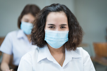 Cheerful college students in classroom wear protective face masks and use antiseptic for coronavirus prevention during coronavirus pandemic. Group of students wearing protection masks in class.