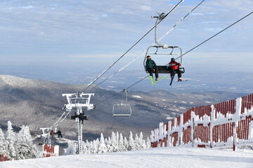 Chairlift with people at Stowe Ski Resort in Vermont, view to the Mansfield mountain slopes,...