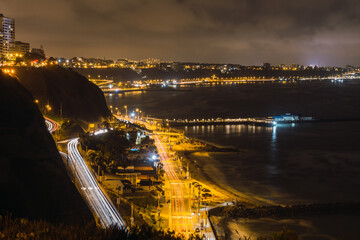 night view of a highway next to the ocean and yellow lights of the city