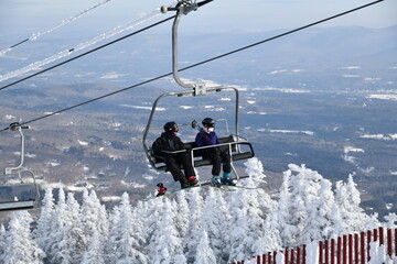 Fototapeta na wymiar Chairlift with people at Stowe Ski Resort in Vermont, view to the Mansfield mountain slopes, December fresh snow on trees early season in VT, hi-resolution image