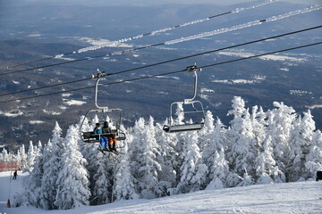 Chairlift with people at Stowe Ski Resort in Vermont, view to the Mansfield mountain slopes, December fresh snow on trees early season in VT,  hi-resolution image