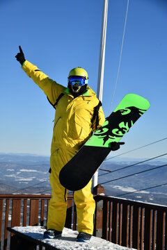Snowboarder wearinig yellow suit posing for photos at sunny day on the top summit of Stowe mountain ski resort, VT 2020.  Hi-resolution image