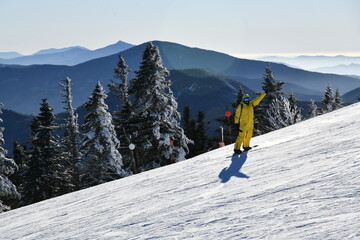 Fototapeta na wymiar Snowboarder riding down the slopes wearing yellow mono suit on sunny day with fresh snow. Stowe mountain ski resort, VT 2020. Hi resolution image