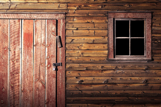 A wooden barn door with a padlock and a window. The wood has some great texture is in good shape. The window shows a very dark interior to the building. 
