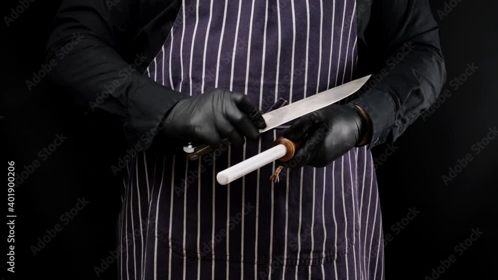 Wall mural chef in black latex gloves and a striped apron sharpens a knife on a ceramic sharpener with a wooden