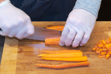 Hands with gloves cutting carrots on a board