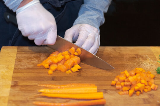 Hands With A Knife And Gloves Cutting Vegetables On A Board