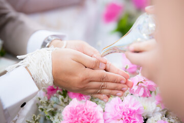 Water pouring in to bless the bride and groom in a Thai wedding ceremony. The groom's hands are resting and placed on the pillow to receive the blessing of relatives or friends.