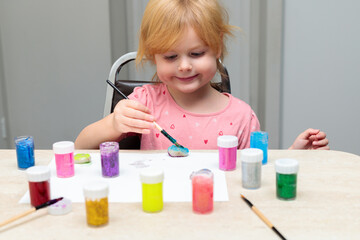 Little smiling child painting pebbles with colorful paints on the table