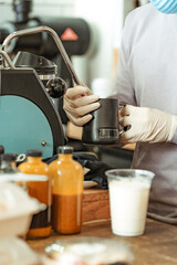 Barista at coffee shop restaurant wearing gloves and mask making drink to-go. New normal, small local business support concept