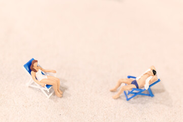 Miniature people , Couple sunbathing together on deck chairs on The beach
