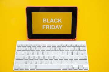 Black Friday text on digital tablet screen with wireless keyboard isolated on yellow background