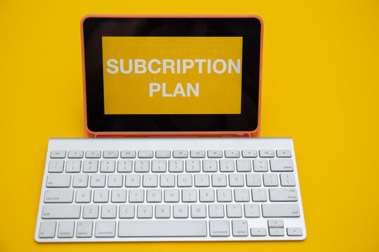 SUBCRIPTION PLAN on digital tablet screen with wireless keyboard isolated on yellow background