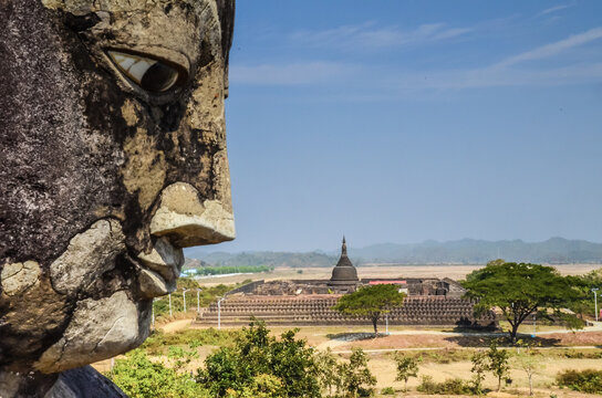 A closeup shot of a stone statue face with temple on background in Mrauk U Myanmar