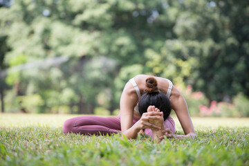 Asian model poses yoga in a park on a natural green background, health care concept, beautiful body structure, fit body