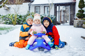 Two little kid boys and cute toddler girl sitting together on sledge. Siblings, brothers and baby sister enjoying sleigh ride during snowfall. Children sledding on snow. Active fun for family vacation