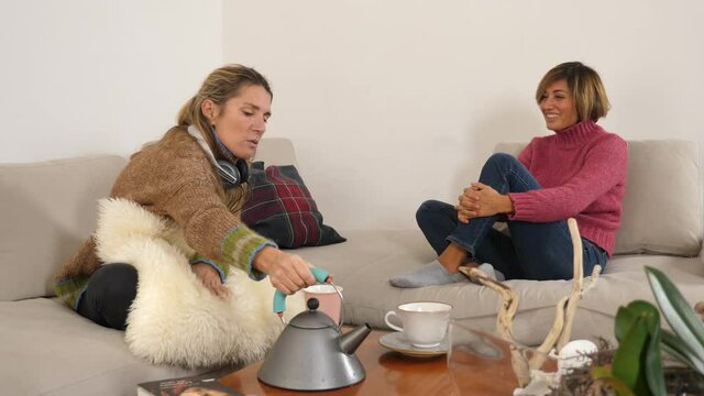 Due donne allegre si divertono durante l'ora del t&egrave; in casa.
Giovani donne felici parlano e ridono mentre bevono un t&egrave; insieme nel soggiorno di casa