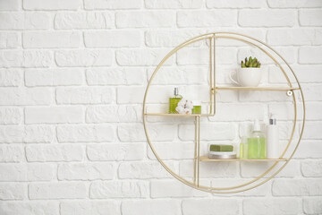 Modern shelf with body care cosmetics and accessories on white brick wall in bathroom