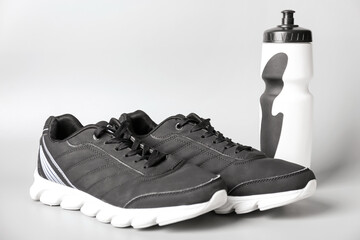 Sportive shoes and bottle of water on white background