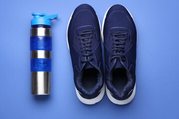Sportive shoes and bottle of water on color background