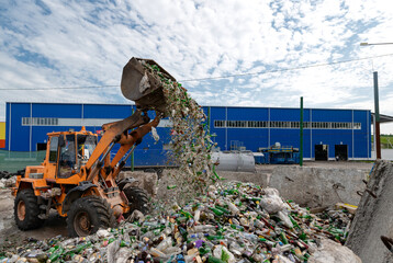 A bucket loader pours broken glass bottles. Disposal of household glass waste